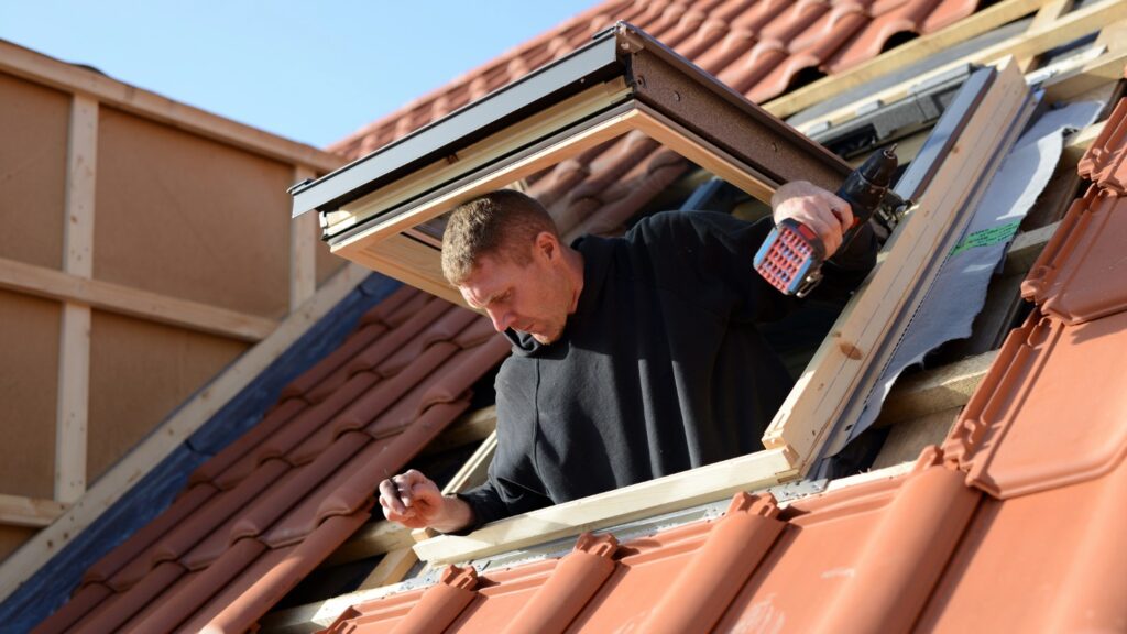 Person installing a skylight in a sloped red tile roof