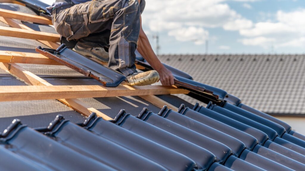 Worker installing roof tiles on a house under a blue sky