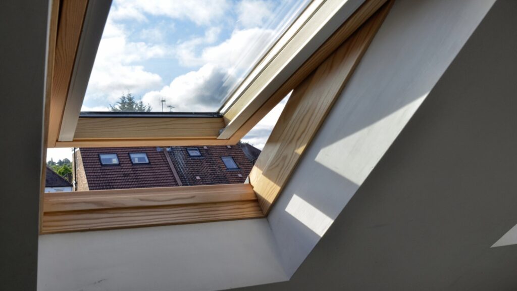 A roof window with a view of the sky and a nearby roof