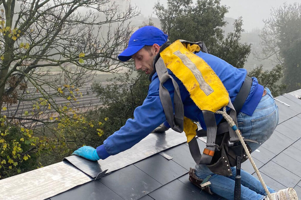 A worker wearing safety gear installs roofing material on a foggy day